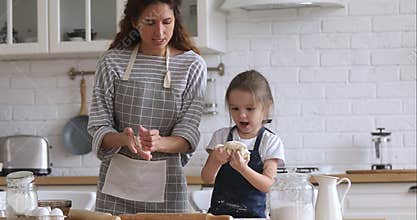 Happy mom teaching kid daughter kneading dough in kitchen together