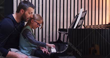 Dad teaching piano to his daughter.Little girl learning piano at home-Side view.Piano class at home. Child learning