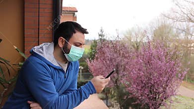 Young caucasian man with mask looking out onto home terrace during quarantine due to coronavirus covid19 pandemic