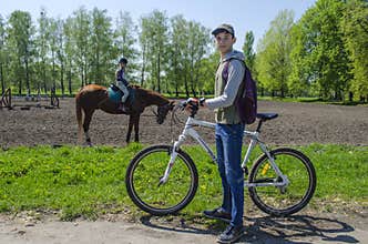 Ukraine, Kiev, April 29, 2018.Teenager boy with a bicycle on the background of a girl riding a horse