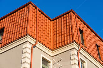 Newly installed construction frame house rain gutter system on the red metal roof top.