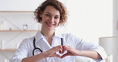 Smiling woman cardiologist showing heart looking at camera