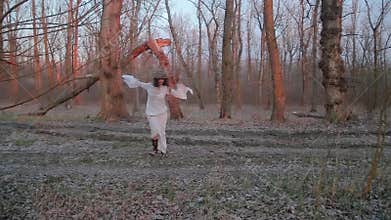 Cute young woman in image of witch and old Slavic costume runs through forest