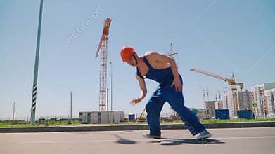 Happy Caucasian Man Builder in Hard Hat Dancing Brakedance. Worker Funny Moves Against the Background of the Construction Site