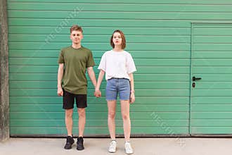 Full-length portrait of a boy and girl holding hands and standing on a green background, looking at the camera and smiling.
