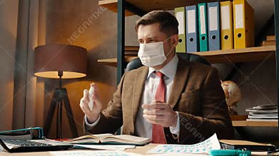 Work during the coronavirus epidemic. A man in a medical mask come to the workplace and uses an antiseptic to disinfect.