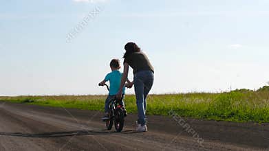 A small child rides a Bicycle with a caring mother who teaches him to ride a Bicycle. Happy family, the concept of an