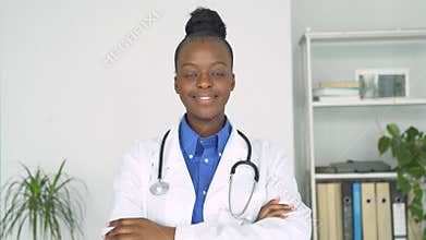 Young adult smiling black female doctor looking at camera standing arms crossed.