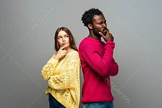 Interracial couple in knitted sweaters standing back to back on grey background
