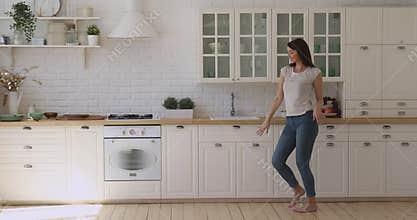 Happy carefree active girl dancing alone in modern kitchen interior