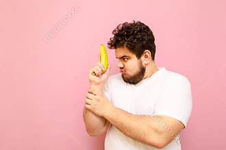 Portrait of a funny fat man isolated on a pink background, playing with a banana in his hand and looking away. Funny young man