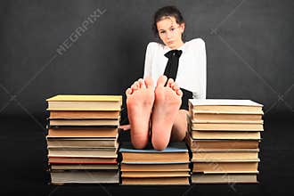 Soles of bare feet of teenage girl on top of old books