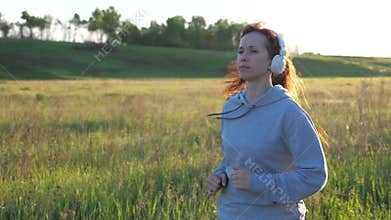 Young woman is training in summer in the park at dawn in headphones with music. Free beautiful girl is engaged in