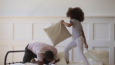 Cute daughter playing pillow fight on bed with black father