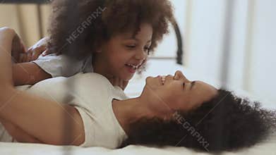 Cute little african child daughter tickling happy mother on bed
