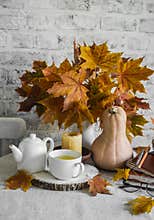 Bouquet of maple leaves, pumpkin, hot tea, lighted candle on the kitchen table.Warm cozy autumn interior