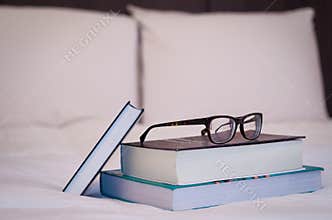 Books on the white bed, glasses on top