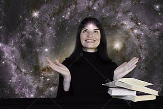 A positive girl in black clothes sits at a table with books against the background of the starry sky