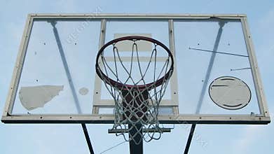 A man`s hand throws the ball into a basketball hoop. Basket with net on sunny summer day close up on background of clear