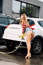 Woman holding pressure washer and smiling near autos