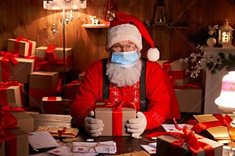 Santa wearing face mask holding Christmas gifts on xmas eve.