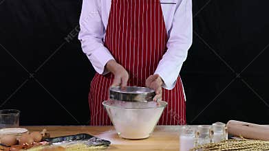 Young Asian chef placing sieve on table after shaking sieve to filter bakery flour