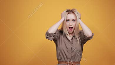 Blonde girl in brown blouse over isolated orange background shows emotions