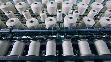 Factory machines spin bobbins, coiling white threads.