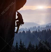 Silhouette of man rock climbing on straight vertical rock at sunrise. Side view. Extreme challenging ascent. Copy space