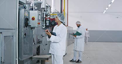 Commercial looking engineer woman in a big bakery industry checking the industrial machine she make some notes in her
