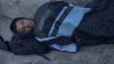 Poor homeless teenager lying street ground covered with sleeping bag, despair