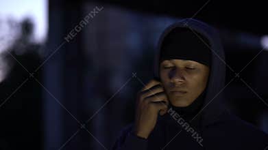 Afro-american bandit putting on balaclava committing crime at night, burglar
