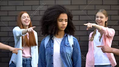Cruel group of teens pointing fingers at curly afro-american schoolgirl, racism