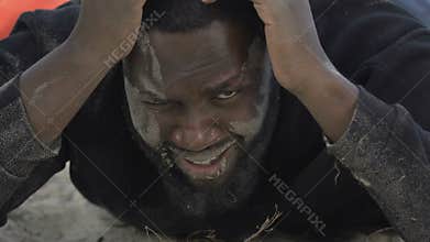 Crying Afro-American man looking at camera on sea coast, catastrophe victim