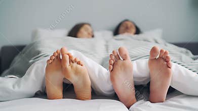 Husband and wife sleeping in bed under blanket together, focus on feet