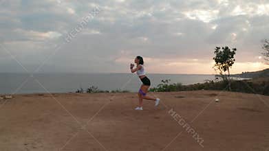 Aerial view of woman exercising on sea shore cliff at sunrise