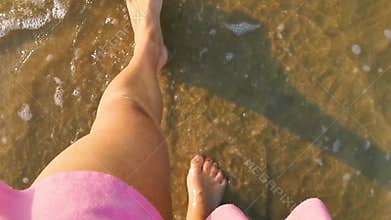 Female in a pink skirt walking with bare feet in the water, waves coming by, relaxation in nature