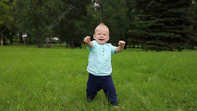 Baby boy`s first steps. The child holds his hands in front of him to keep balance
