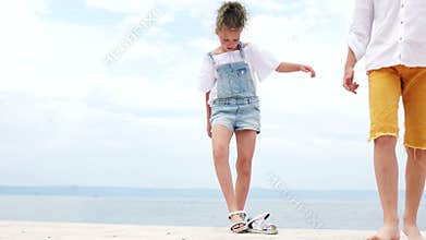 Girl and boy standing on a sea berth. Girl takes off her sandals and goes barefoot, summer vacation, happy children