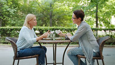 Beautiful middle-aged women chatting holding coffee cups in outdoor cafe