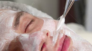 Sliding shot of a man getting facial mask applied by cosmetologist at spa center