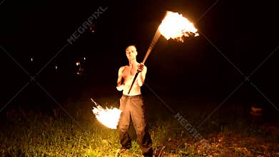 Slow motion of a young man in black pants in total darkness shows a representation of a rotating burning torch