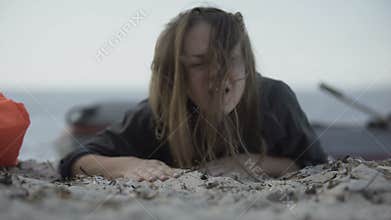 Woman coughing heavily, barely crawling on sand, surviving natural catastrophe