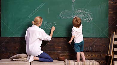 Nursery teacher and child boy painting picture on chalkboard. Woman and boy draw. Mother and son draw with chalk at