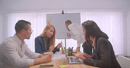 Portrait of four collleagues meeting and having a discussion on the workplace indoors. Businessman drawing a graph on