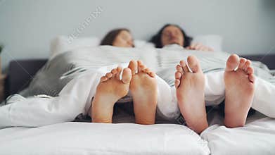 Woman and man couple lying in bed together sleeping under blanket, focus on feet