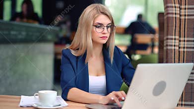 Confident beautiful young business female working in cafe looking at screen of laptop