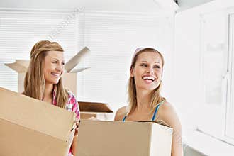 Laughing female friends holding boxes after moving
