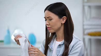 Sad housewife holding shirt with coffee stain, laundry problems, spot remover
