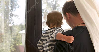Anonymous father and baby looking out window